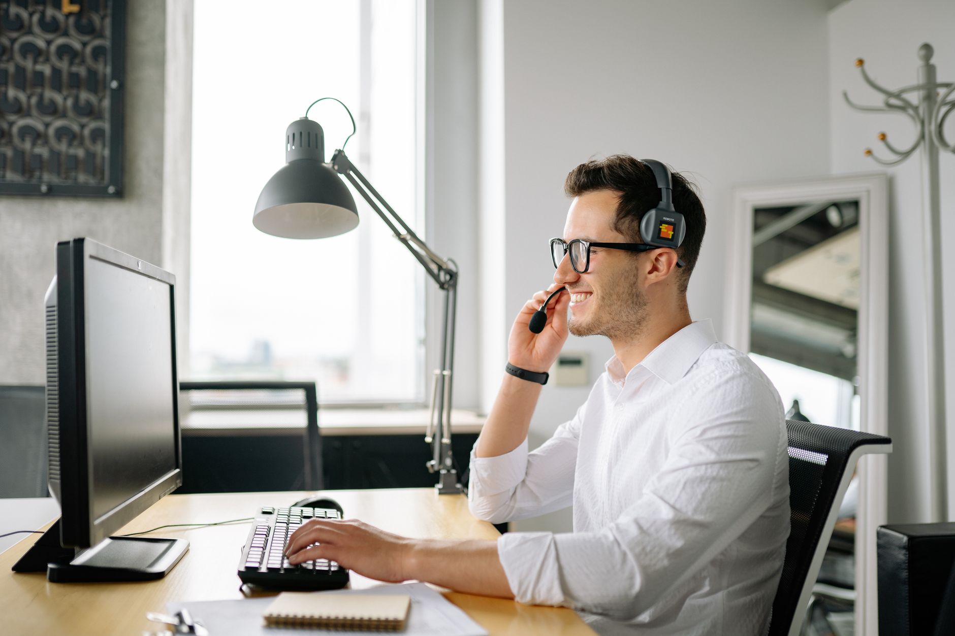 Smiling man wearing headset working at computer in bright office — illustrating: VoIP vs Traditional Phone Systems in Central Florida: Which Saves SMBs More Money in 2024?